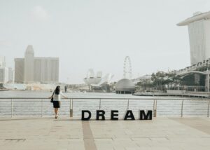 Home A woman gazing at the iconic Marina Bay Sands skyline in Singapore with 'Dream' letters foregrounded.