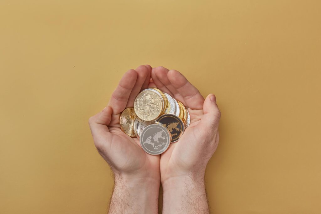 Close-up of hands holding various cryptocurrency coins over a yellow background, highlighting modern digital finance.