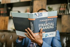 Home A professional individual in a suit reading 'Fundamentals of Financial Planning' indoors.